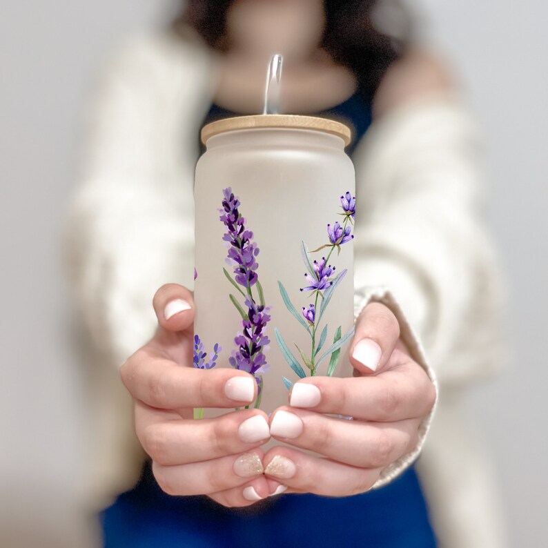 May include: A frosted glass water bottle with a bamboo lid and a straw. The bottle has a lavender floral design.