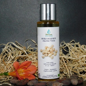 May include: A clear glass bottle with a silver cap filled with a light yellow liquid. The bottle label is white with blue text that reads "PUR SENS HUILE DE KUKUI Aleurites Triloba". The label also includes information about the oil, including that it is 100% pure and natural, the lot number, the origin (Madagascar), and that it is cold-pressed. The bottle is sitting on a bed of shredded brown paper.