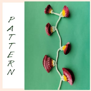 Puede incluir: Una vid floral de ganchillo con cinco flores en tonos burdeos, rosas y amarillos. Las flores están conectadas por un tallo de ganchillo blanco sobre un fondo verde. La palabra "PATTERN" está escrita verticalmente en letras verdes.