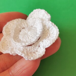 May include: A white crocheted flower with multiple layers. The flower is made with a single crochet stitch and has a delicate, feminine look.