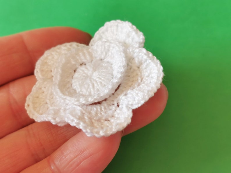May include: A white crocheted flower with multiple layers. The flower is made with a single crochet stitch and has a delicate, feminine look.