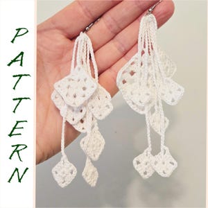 May include: A pair of white crochet earrings with a cascading design. Each earring has square and diamond-shaped crochet elements, suspended from a silver hook. The word "PATTERN" is written vertically in green on the left side.