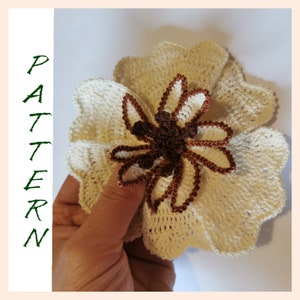 May include: A crocheted flower with a brown center and white petals. The flower is made with a delicate stitch and has a layered design.
