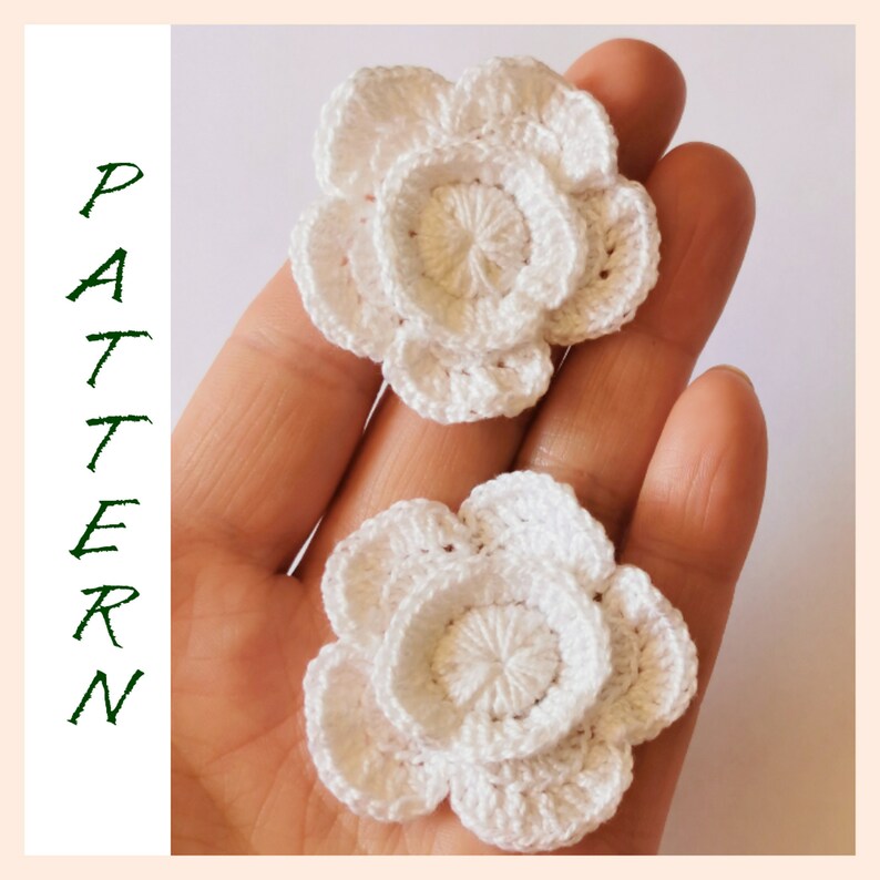 May include: Two white crocheted flowers with multiple layers of petals. The flowers are delicate and intricate.