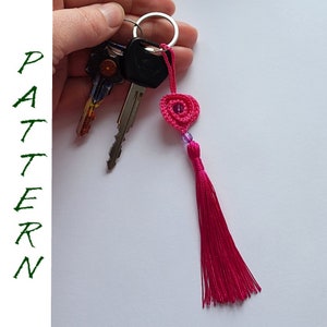 May include: A pink crocheted heart charm with a purple bead and a pink tassel attached to a silver key ring.