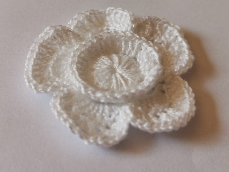 May include: A white crocheted flower with multiple layers of petals.