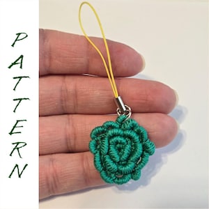 May include: A teal-colored, handmade charm in the shape of a rose. The charm is attached to a yellow cord with a silver-colored metal clasp. The word "PATTERN" is written vertically in green letters.