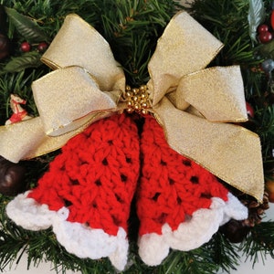 May include: A red crocheted bell ornament with white trim, tied with a gold ribbon bow, on a green Christmas wreath.