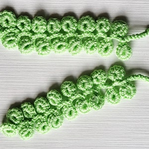 May include: Two crocheted green leafy sprigs with a delicate, lacy texture. The sprigs are made of yarn and have a natural, organic look.