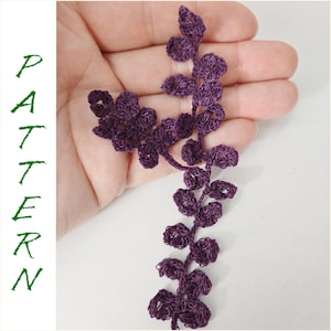 Puede incluir: Una guirnalda de hojas de ganchillo de color morado con un diseño delicado e intrincado. La guirnalda presenta múltiples hojas conectadas por un tallo delgado.