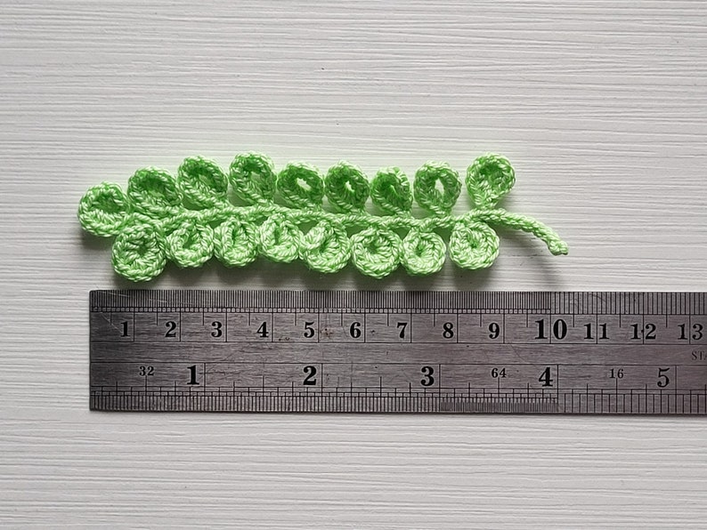 May include: A green crocheted leaf measuring approximately 10 cm long. The leaf is made of small, looped stitches and has a delicate, lacy appearance.