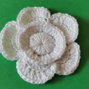 May include: A white crocheted flower with multiple layers of petals.