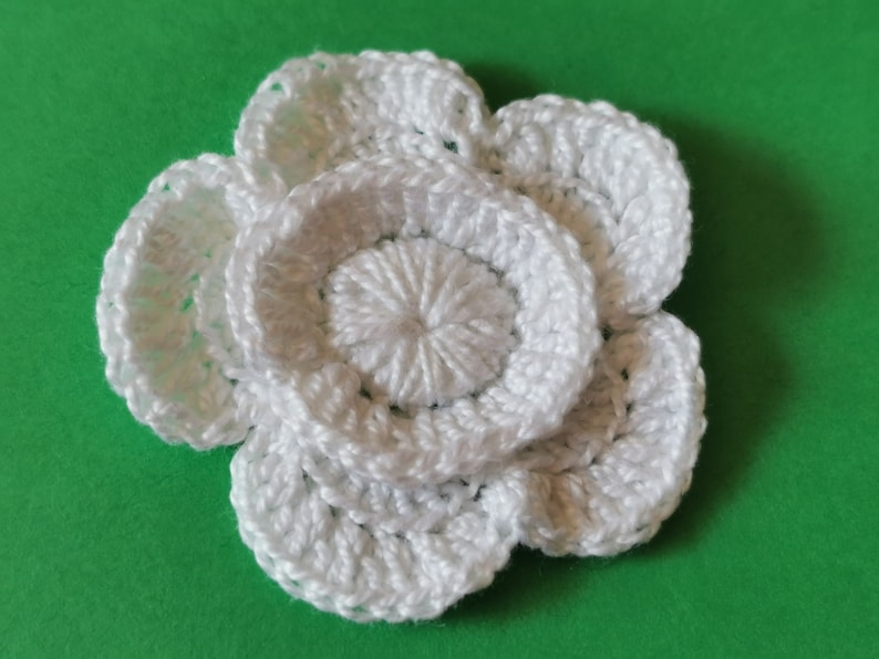 May include: A white crocheted flower with multiple layers of petals.