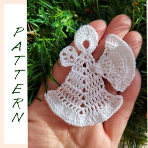 May include: White crocheted angel ornament with a halo and wings. The angel is held in a hand against a green background.