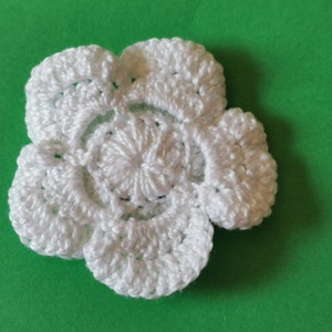 May include: A white crocheted flower with five petals. The flower is made with a delicate stitch pattern and has a raised center.