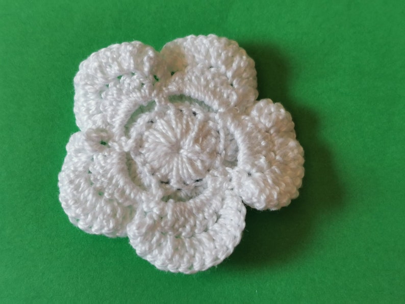 May include: A white crocheted flower with five petals. The flower is made with a delicate stitch pattern and has a raised center.