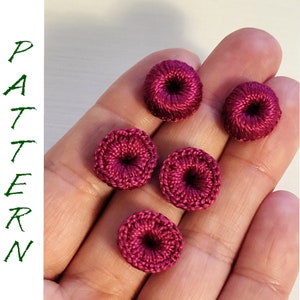 Pode incluir: Cinco pequenas decorações em forma de donut, de cor bordô, feitas de crochê.