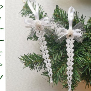 Puede incluir: Dos adornos navideños de crochet blanco con lazos blancos y tul blanco. Los adornos están colgados de un árbol de Navidad verde.