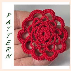 Puede incluir: Una flor roja hecha a crochet con un diseño delicado e intrincado. La flor está hecha con un solo hilo de lana y tiene una forma circular.