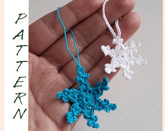 May include: Two crocheted snowflakes, one white and one turquoise blue, hanging from white string. The snowflakes are in the palm of a hand.