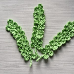 May include: Three crocheted green fern sprigs with rounded leaves.