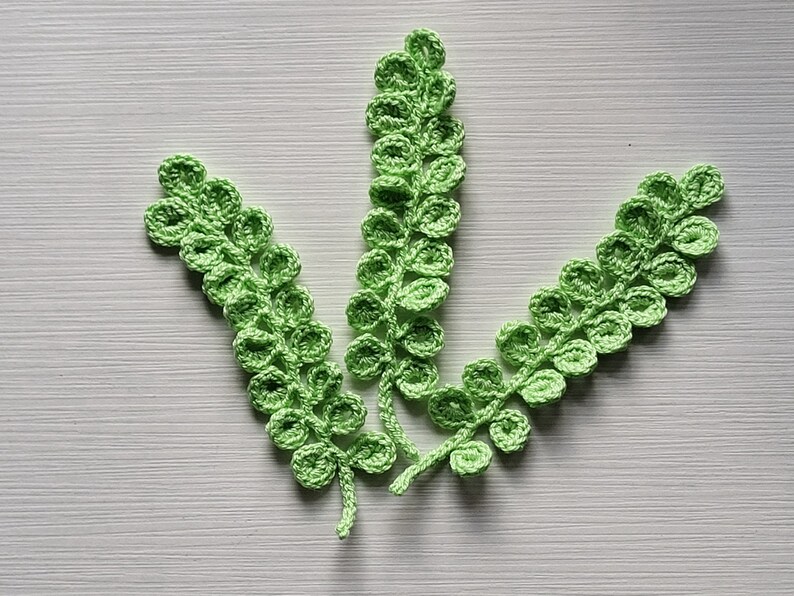 May include: Three crocheted green fern sprigs with rounded leaves.