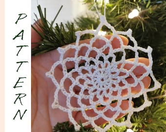 Puede incluir: Adorno de copo de nieve blanco tejido a crochet colgado de un árbol de Navidad. El copo de nieve es delicado e intrincado, con un diseño en espiral en el centro.