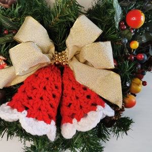 May include: A Christmas wreath decorated with red and white crocheted bells, a gold bow, and various red and brown berries.