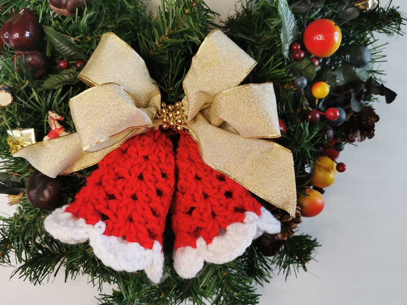 May include: A Christmas wreath decorated with red and white crocheted bells, a gold bow, and various red and brown berries.