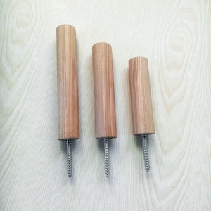 May include: Three wooden dowels with a screw at the bottom. The dowels are different lengths and are arranged in a row from left to right, with the longest dowel on the left and the shortest dowel on the right.