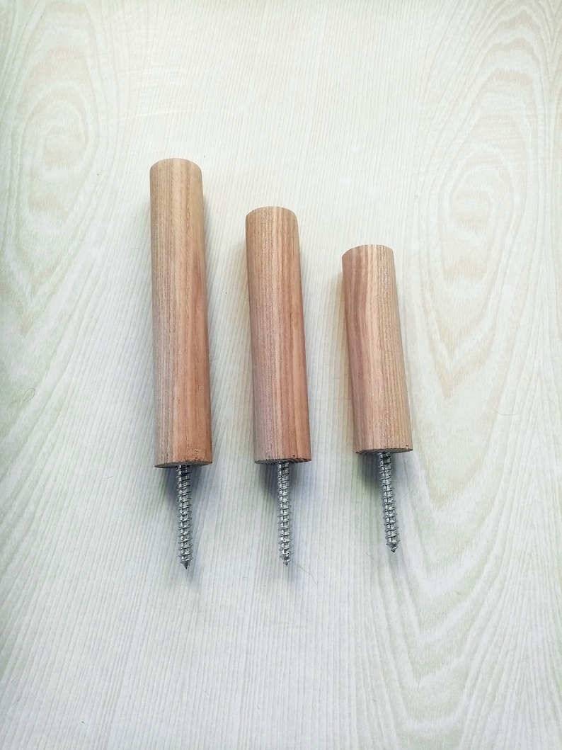 May include: Three wooden dowels with a screw at the bottom. The dowels are different lengths and are arranged in a row from left to right, with the longest dowel on the left and the shortest dowel on the right.