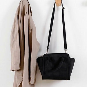 May include: A brown shirt hanging on a wooden hook next to a black handbag with a shoulder strap.
