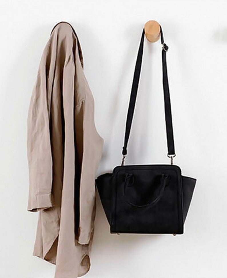 May include: A brown shirt hanging on a wooden hook next to a black handbag with a shoulder strap.