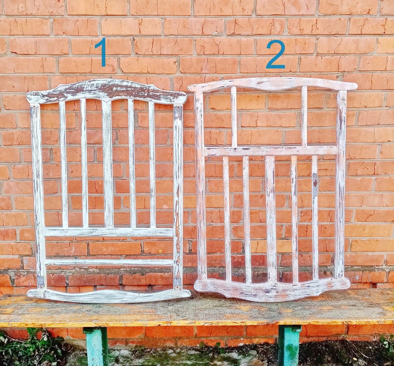 May include: Two white painted wooden frames with a slatted design. The frames are labeled "1" and "2" and are sitting on a wooden bench.
