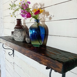 May include: A rustic wooden shelf with black metal brackets, decorated with a blue glass vase filled with wildflowers and ceramic jars.