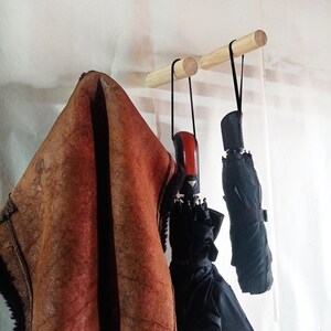 May include: Two wooden wall hooks with a brown leather jacket and two black umbrellas hanging from them.