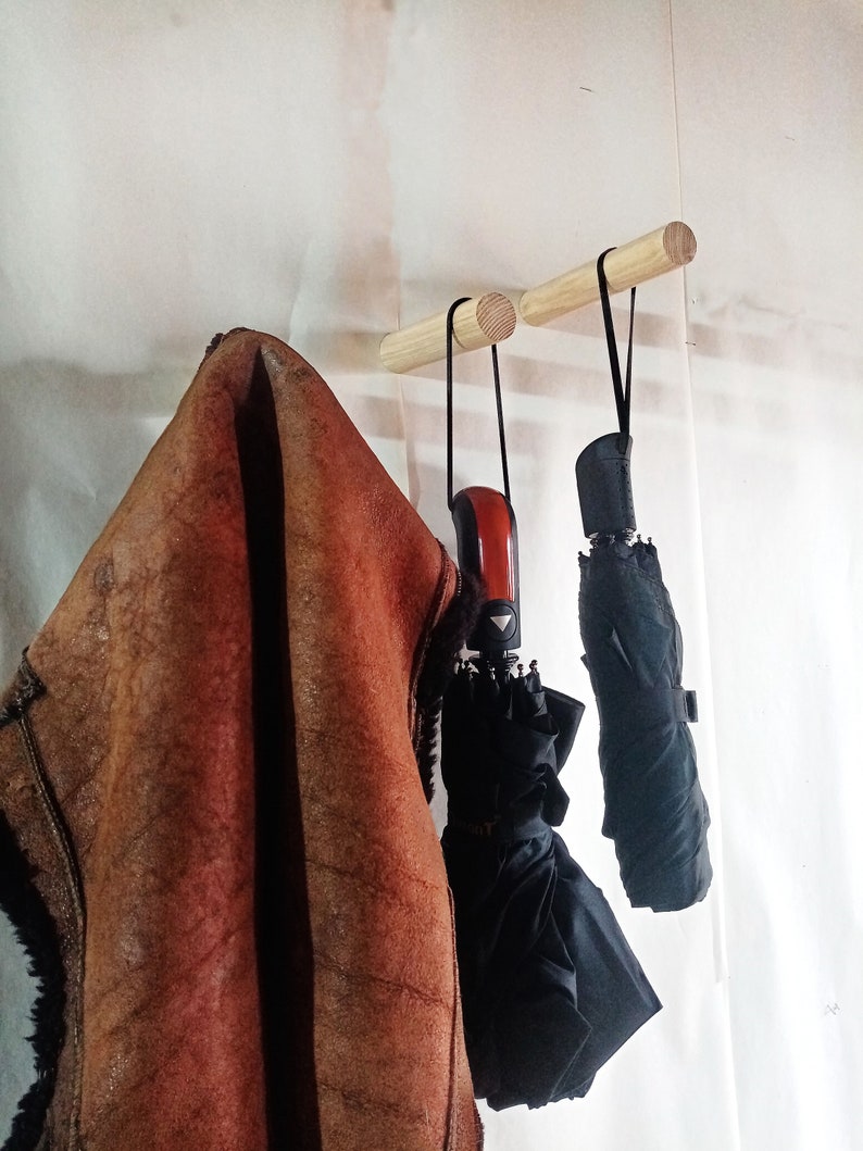 May include: Two wooden wall hooks with a brown leather jacket and two black umbrellas hanging from them.