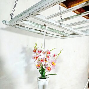 May include: White wooden hanging shelf with a white pot and pink and white orchid flowers hanging from it.