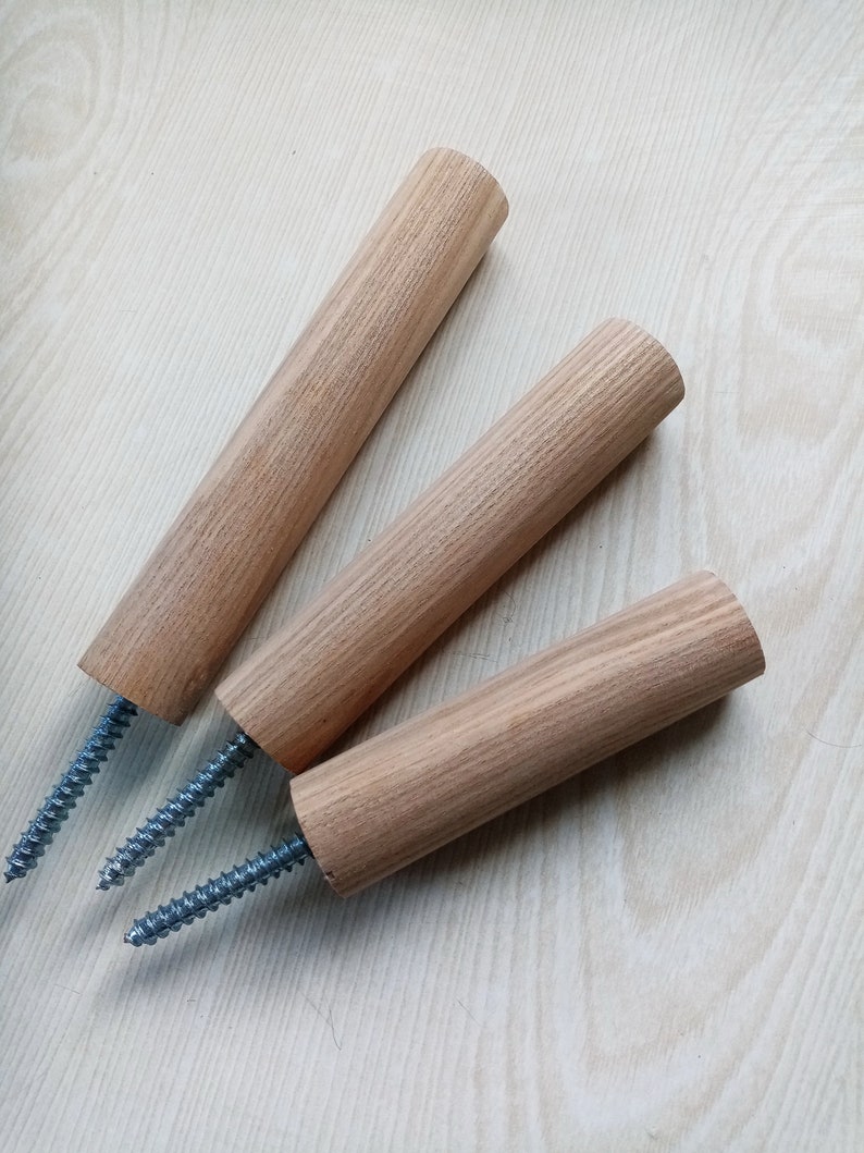 May include: Three wooden dowels with metal screws attached. The dowels are light brown and have a wood grain pattern. The screws are silver and have a threaded design.