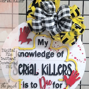 May include: A white round wooden sign with yellow and red paint splatters. The sign has black text that reads "My knowledge of Serial Killers is to Die for". There are red handprints on the sign. The sign is decorated with a black and white checkered bow and yellow caution tape.
