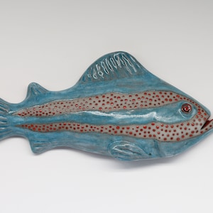 Könnte beinhalten: Eine Keramik-Fischskulptur mit blauer Glasur und roten Akzenten. Der Fisch hat ein gestreiftes Muster und eine gepunktete Textur.