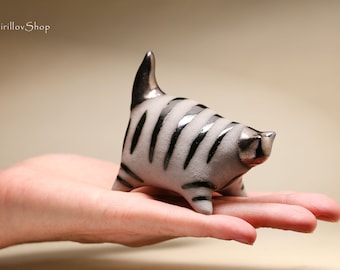 May include: A small ceramic cat figurine with black and white stripes. The cat is standing on its hind legs with its tail raised in the air. The figurine is painted in a glossy white glaze with black stripes.