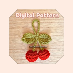 Puede incluir: Un patrón de crochet para un amuleto de cereza con hojas verdes. El amuleto está hecho con hilo rojo y verde y es perfecto para agregar un toque de fantasía a cualquier proyecto.