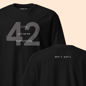 Peut inclure: Un t-shirt noir à manches courtes avec un grand chiffre 42 gris sur le devant, accompagné des mots life, universe et everything imprimés en blanc. Le dos du t-shirt affiche le texte don't panic en petite police blanche centré en haut.