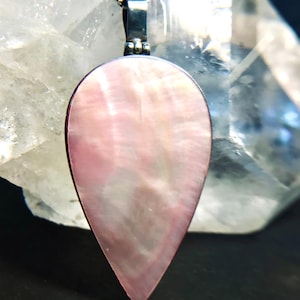 May include: A pear-shaped pendant necklace with a pink mother-of-pearl inlay. The pendant is framed in silver-coloured metal and hangs from a delicate chain. The iridescent surface of the inlay reflects light, creating a subtle shimmer. The necklace is a piece of jewellery.