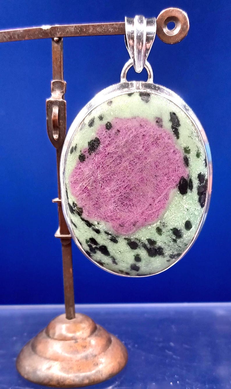 Pu&ograve; includere: Ciondolo ovale con castone color argento. Il ciondolo presenta un'area rosa centrale circondata da una base verde chiaro con macchie nere. &Egrave; sospeso da un'ansa color argento.