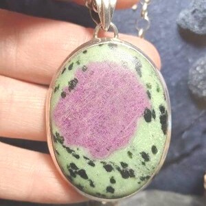 Pu&ograve; includere: Collana con pendente ovale color argento. Il pendente presenta un grande centro rosa strutturato, circondato da un bordo verde chiaro con macchie nere. Il pendente &egrave; racchiuso in una cornice di metallo color argento.