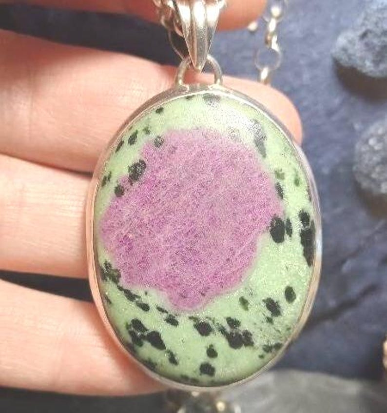 Pu&ograve; includere: Collana con pendente ovale color argento. Il pendente presenta un grande centro rosa strutturato, circondato da un bordo verde chiaro con macchie nere. Il pendente &egrave; racchiuso in una cornice di metallo color argento.