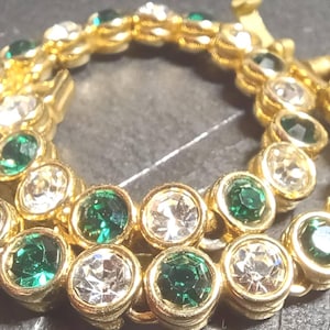 May include: A gold-toned bracelet with alternating emerald green and clear crystal stones. The stones are set in individual bezels, creating a sparkling, elegant accessory. The bracelet is likely for special occasions.