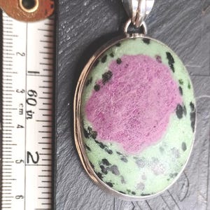 Pu&ograve; includere: Ciondolo ovale con anello argentato. Il ciondolo presenta una grande area rosa centrale circondata da pietra verde e macchiata di nero. Il ciondolo &egrave; lungo circa 5 cm.